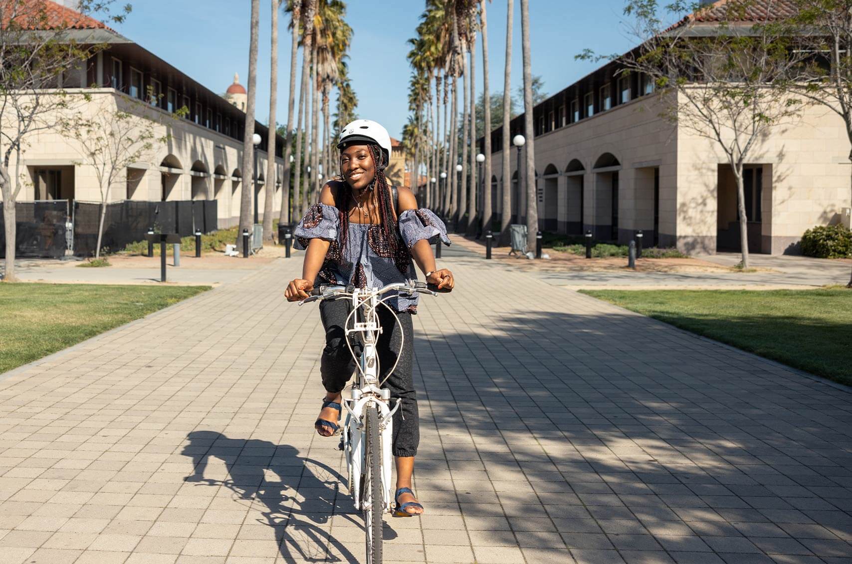 Female student riding bike on Stanford campus, coming right at camera.