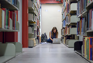 A person working on a laptop, seated on a library floor